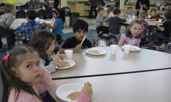 young students eating pancakes at a table in the school
