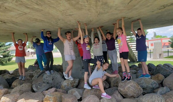 students underneath a bridge, pretending to hold it up