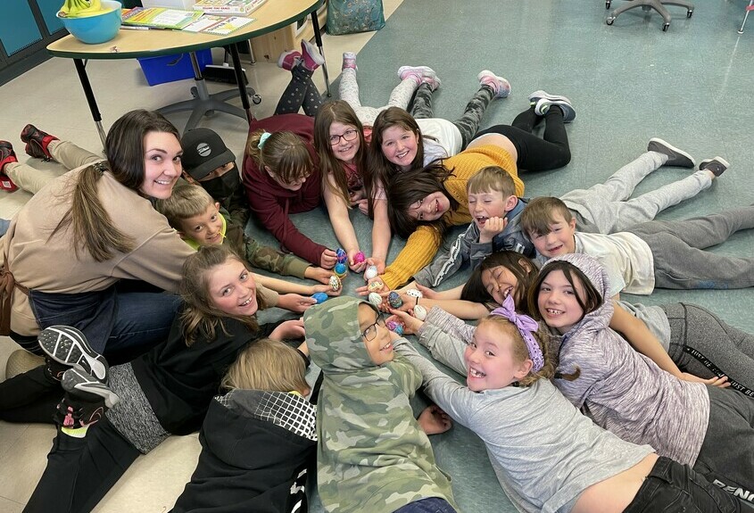 a group of students and their teacher laying on the classroom floor in a circle smiling at the camera